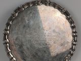 une assiette ancienne en argent, portant une inscription sur une surface grise