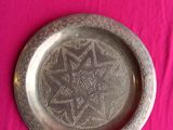 a silver plate with a design on it on a pink surface