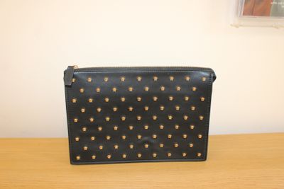un sac à main noir et doré clouté, posé sur une table en bois devant une fenêtre
