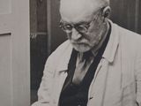 a black and white photo of an older man cutting a cake