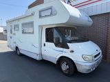 un petit camping-car blanc garé devant un immeuble en briques
