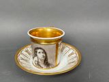 gold and white cup and saucer with a picture of a woman on it