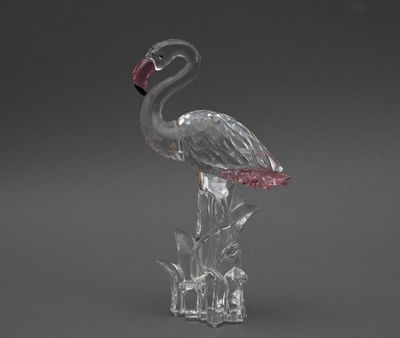 une figurine de flamant rose en verre transparent, dotée d'un bec rose, posée sur un socle transparent