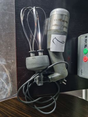 a blender with a whisk on it next to a cup of coffee