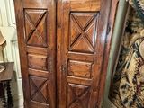 a tall wooden cabinet with two doors and a vase on top of it