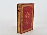 an old red book with a cross on it sitting on a white surface