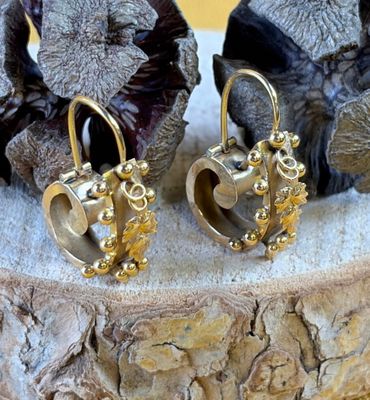 a pair of gold earrings sitting on top of a piece of wood