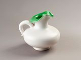 a small white vase with a green leaf on top of it