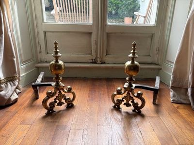 une paire de bougeoirs anciens en laiton posés sur un parquet devant une fenêtre