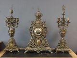 trois bougeoirs dorés et une horloge posés sur une table