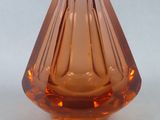 un petit vase en verre orange posé sur une surface blanche