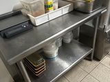 a kitchen with a metal table and a metal shelf with dishes on it