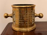 a brass vase on a wooden table with a white wall in the background
