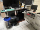 a desk with a computer, printer, and a stool in a room