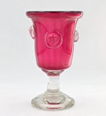 un vase en verre rose muni d'une anse, posé sur un socle