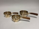 three brass measuring cups with wooden handles on a white surface