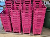 Plusieurs paniers en plastique roses sont empilés les uns sur les autres dans un magasin.