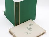 un livre ouvert posé sur une table blanche, à côté d'une boîte verte