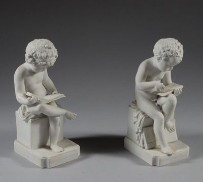 une paire de statues blanches représentant un garçon et une fille assis sur un banc