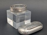 un récipient en verre muni d'un couvercle en argent, à côté d'un comprimé argenté
