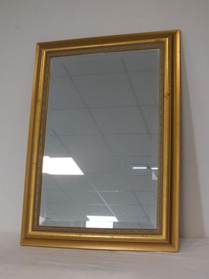un miroir à cadre doré posé sur une étagère dans une pièce aux murs blancs