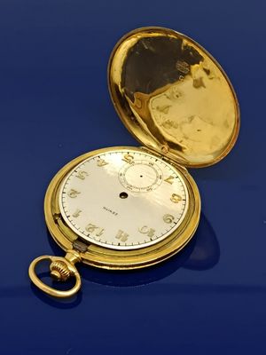 une montre de poche en or posée sur une table bleue