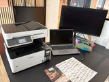 une imprimante et un ordinateur portable posés sur un bureau, à côté d'un écran