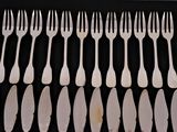 six forks and six knives are arranged in a row on a black surface