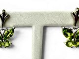 une paire de boucles d'oreilles papillon en péridot, présentées sur un socle blanc