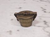 an old brass container with a handle sitting on a white surface