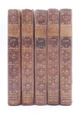 six old books are lined up in a row on a white surface