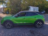 the green suv is parked on the gravel near a trailer