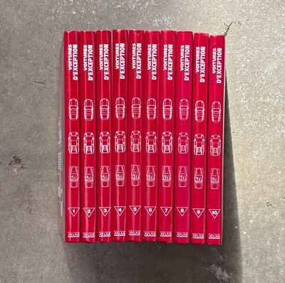 six livres rouges posés sur une surface en béton, sur fond blanc