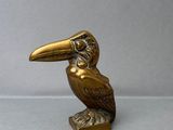 statue en laiton représentant un oiseau posé sur un socle, sur fond gris