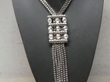 Le collier est en métal argenté et comporte une longue chaîne.
