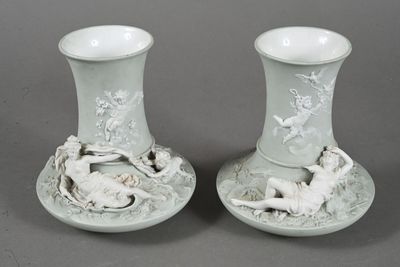 pair of white vases with figures on them sitting on a table