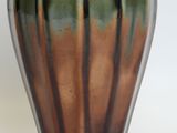 a green and brown vase sitting on a white surface