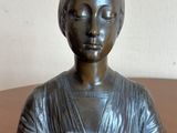 buste en bronze d'une femme posé sur une table en bois, avec un mur blanc en arrière-plan