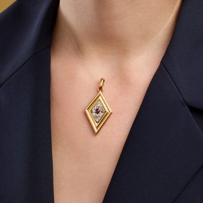 a close up of a woman wearing a gold necklace with a red and white diamond