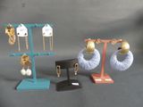 Trois paires de boucles d'oreilles sont présentées sur un présentoir, sur un fond gris.