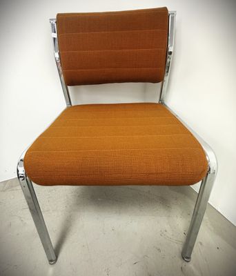 an orange chair with chrome legs and a seat that is up against a wall