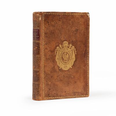 un vieux livre orné d'un emblème doré posé sur une surface blanche