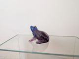 purple frog figurine sitting on a glass table with a white background