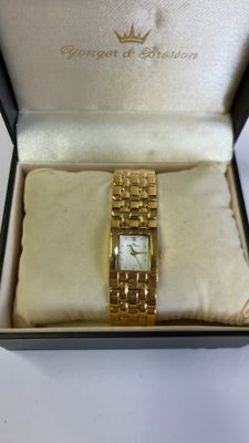 une photo d'une montre en or dans un écrin, posée sur une surface blanche