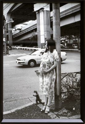 photographie en noir et blanc d'une femme appuyée contre un poteau, à côté d'un chien