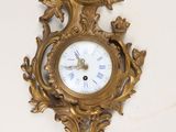 a gold clock on the wall with a white background