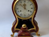 a red and gold clock on a stand on a white background