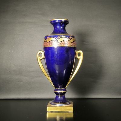 un vase bleu posé sur une table, muni d'une anse dorée