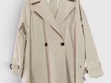Le trench-coat est suspendu à un cintre accroché à un mur blanc.