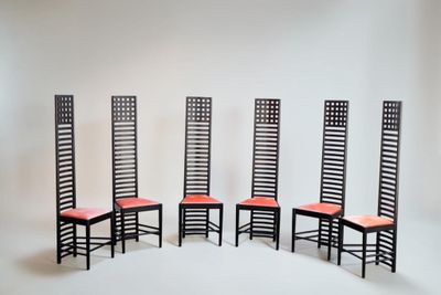 quatre chaises noires avec des coussins rouges sont adossées à un mur blanc